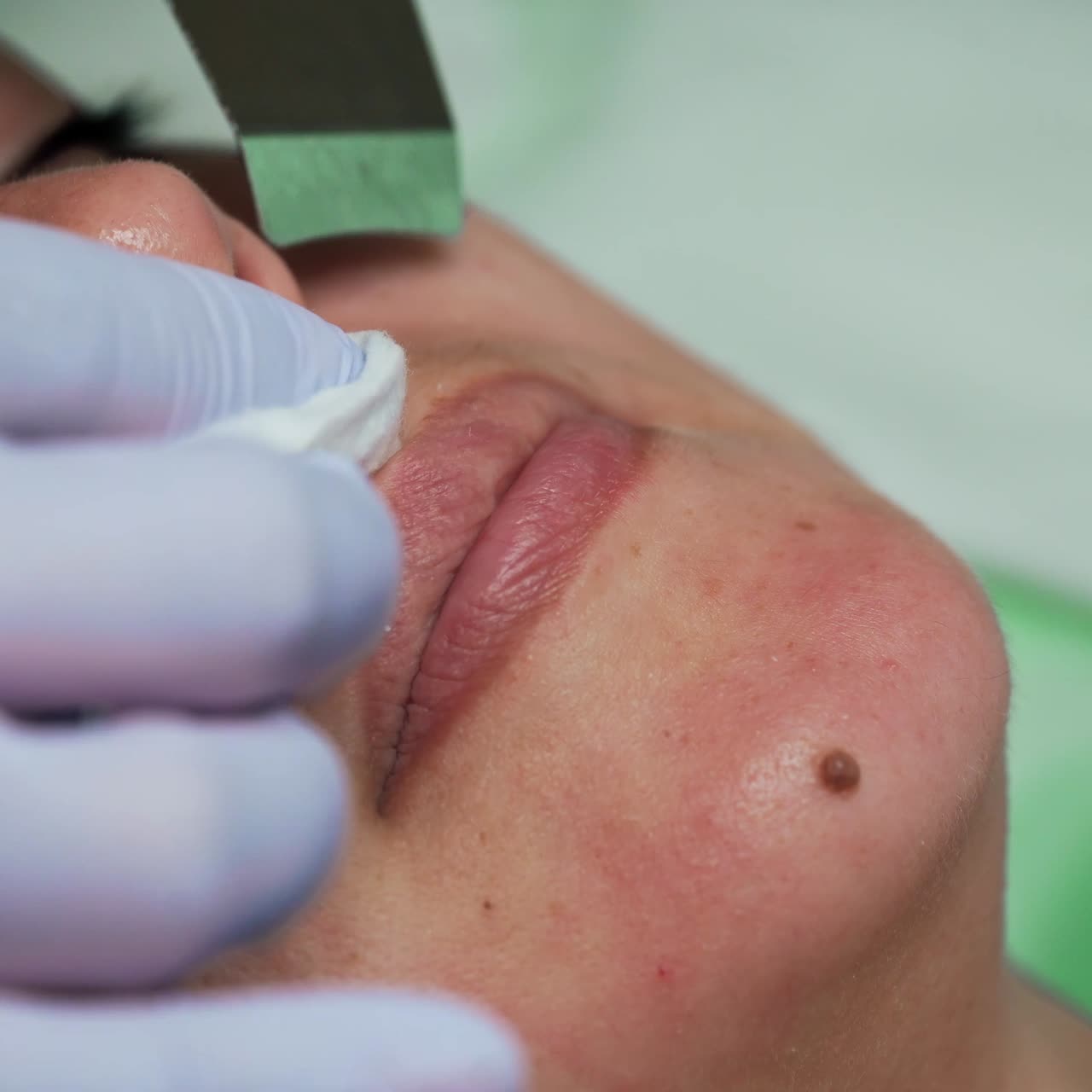 Gloved hands of beautician move ultrasonic scrubber by the face of Caucasian woman. Salon skincare concept. Extreme close up