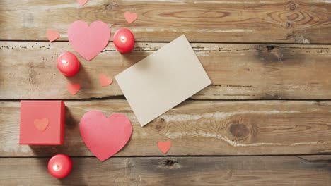 paper hearts and gift with candles on wooden background at valentine's day