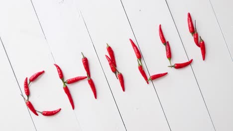 a word chilli formed with small red chilli peppers  placed on white wooden table