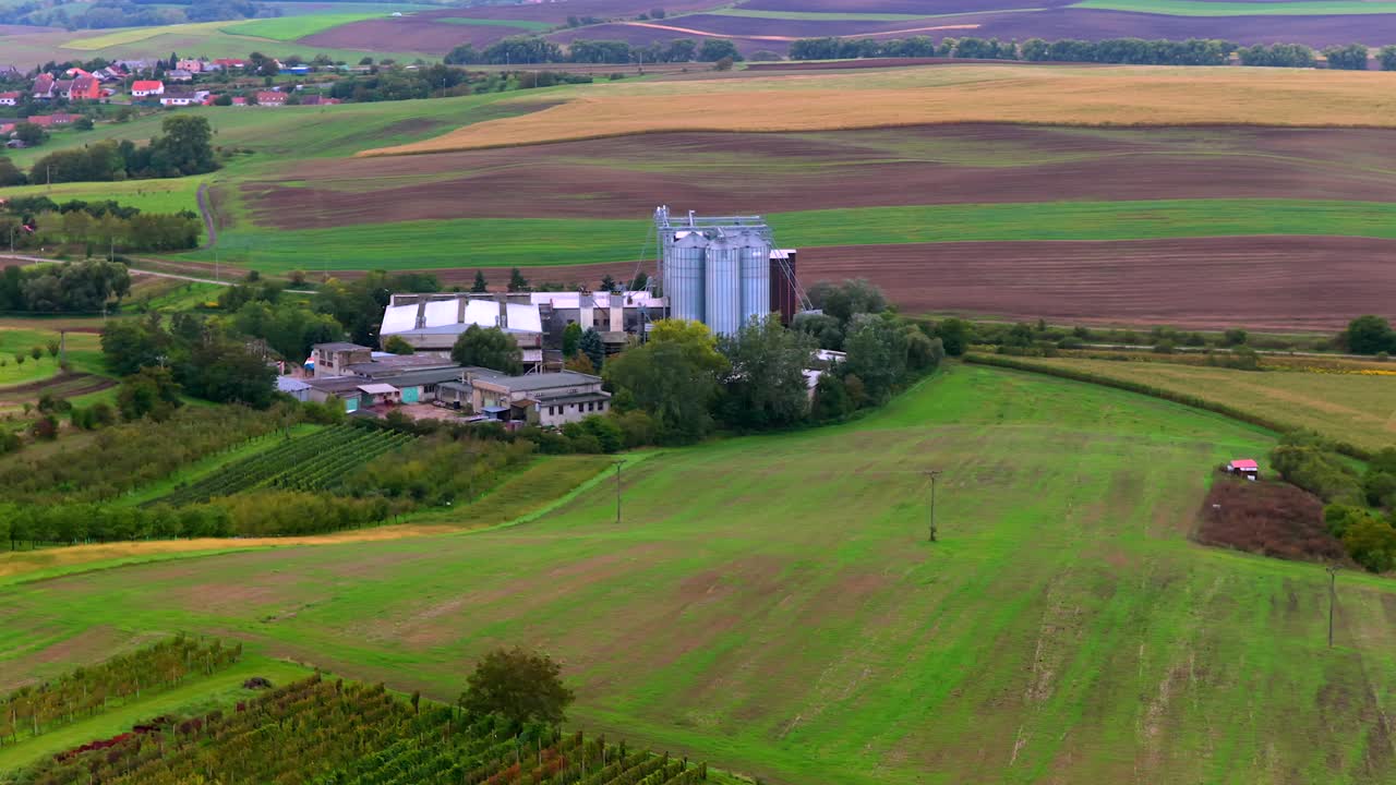 Aerial wide shot of South Moravian farmland fields and vineyards in autumn season. Farmstead with silo strange and colored fields. Small village in distance