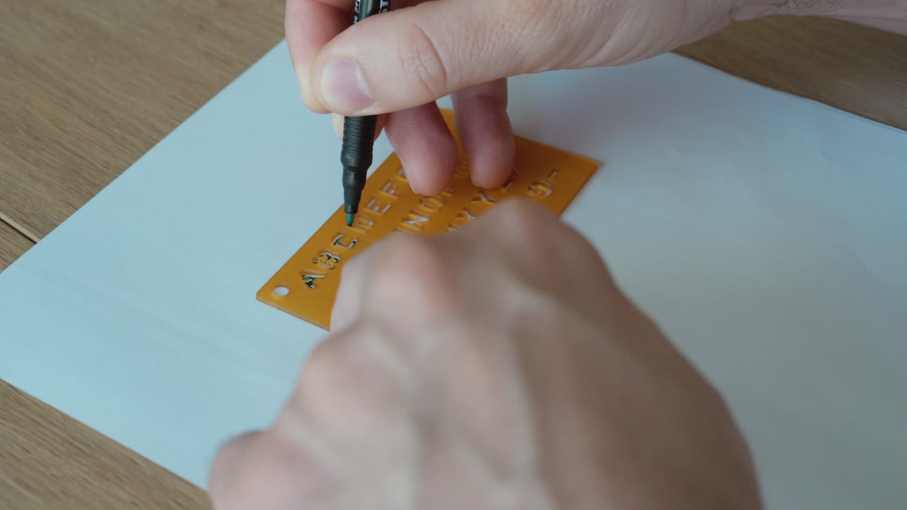 Primo piano di una mano che usa uno stencil e una penna per disegnare lettere, simboleggiando precisione, apprendimento e creatività