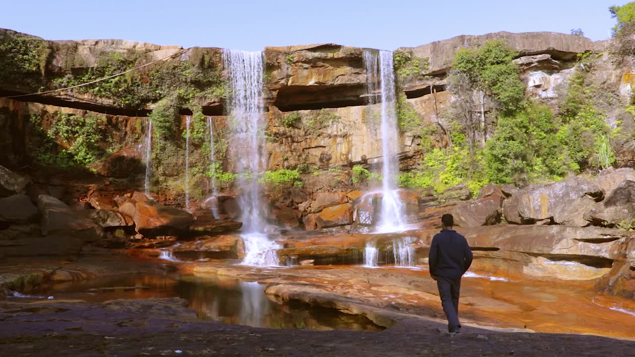 joven disfrutando de la prístina cascada natural que cae desde la cima de la montaña en el día desde un video de ángulo bajo tomado en phe phe fall meghalaya india