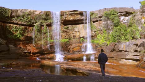 Junger-Mann,-Der-Den-Unberührten-Natürlichen-Wasserfall-Genießt,-Der-Tagsüber-Von-Der-Bergspitze-Fällt,-Aus-Einem-Niedrigen-Winkelvideo,-Das-Bei-Phe-Phe-Fall-Meghalaya-Indien-Aufgenommen-Wurde