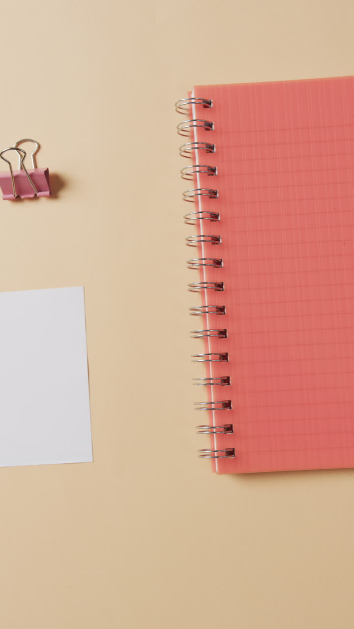 Vertical video of overhead view of school stationery on beige background, in slow motion