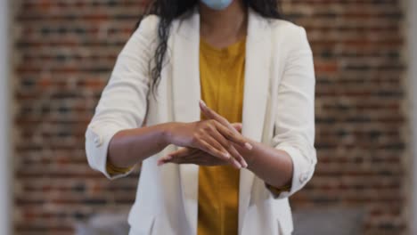 Mid-section-of-woman-sanitizing-her-hands-at-office