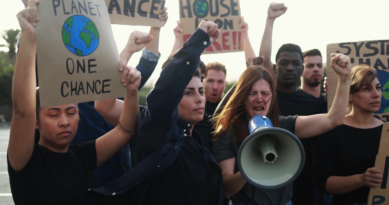 Gruppo eterogeneo di attivisti che protestano contro il cambiamento climatico con megafono e cartelli.