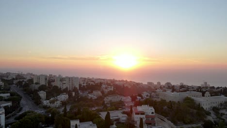 view of the sunset over the hilly and quiet city with tall buildings and the sea horizon, haifa, israel