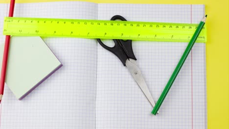 un conjunto de suministros escolares están dispersos en diferentes direcciones en un lugar con un cuaderno en un fondo amarillo pastel