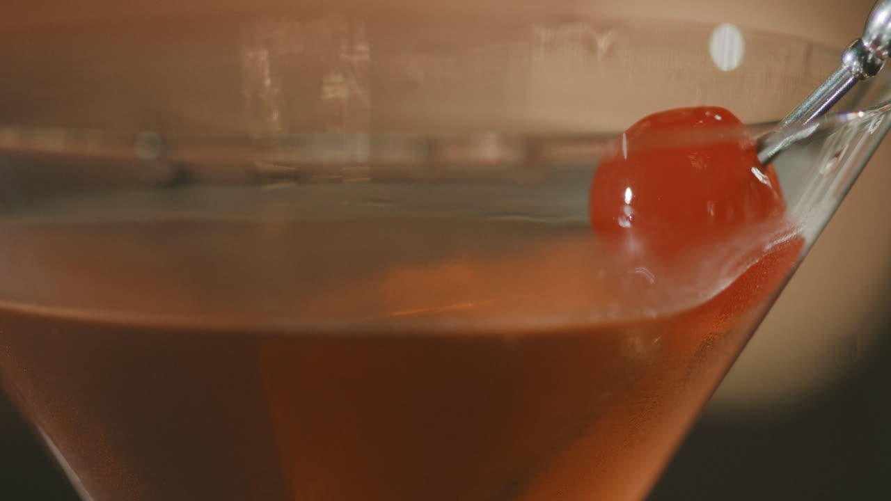 Close-up of an elegant martini glass with a red cherry pierced by a metal toothpick.