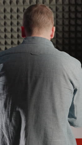 back shot of a man in a blue shirt playing a white piano, with his shadow cast on a black acoustic wall. the scene captures the contrast and texture in a music studio setting