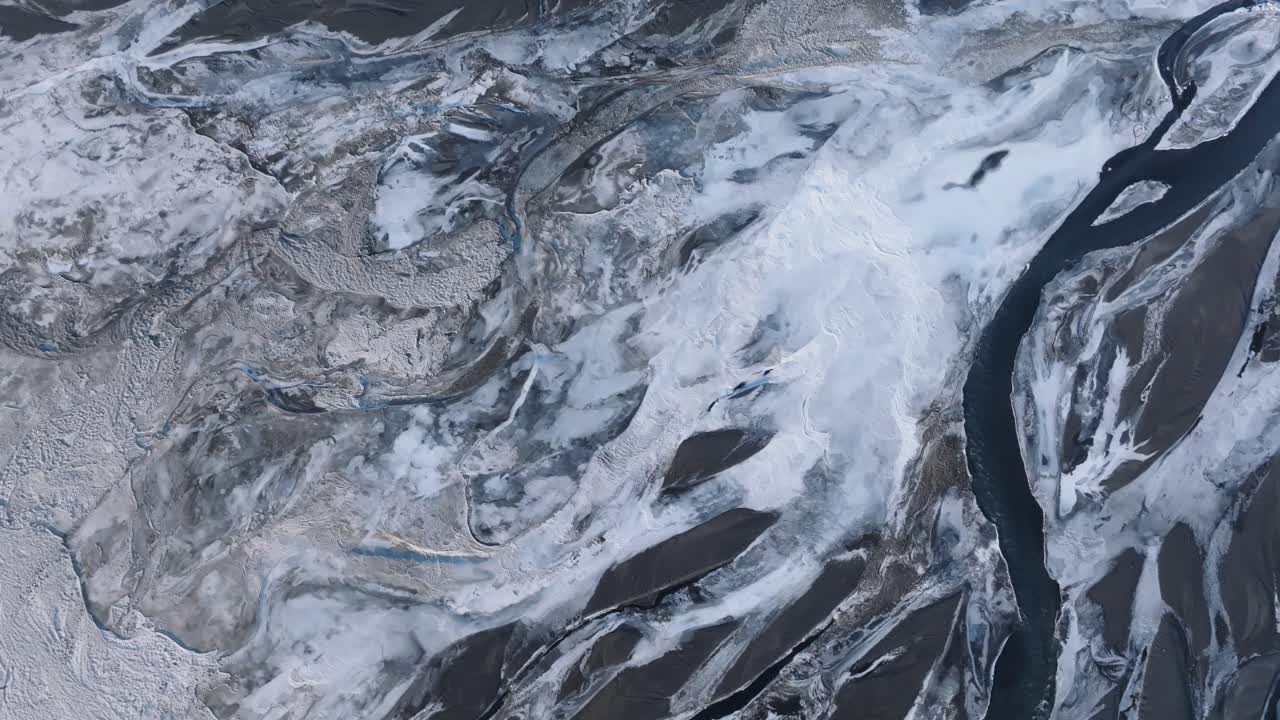 アイスランドの凍った川の湾曲部と雪に覆われた地形上をゆっくりと回転するドローンからの眺め