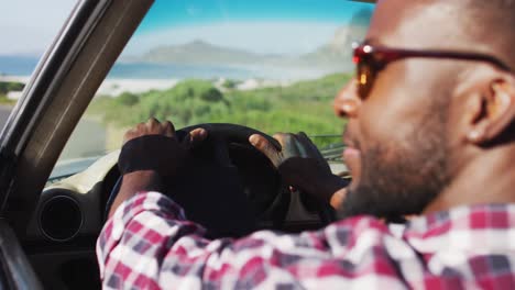 African-american-man-with-hands-on-steering-wheel-sitting-in-the-convertible-car-on-road