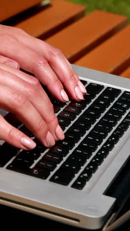 mujer sentada en un banco del parque usando una computadora portátil