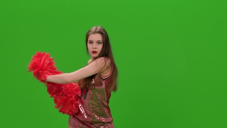 retrato de una animadora feliz bailando con pompones rojos en el estudio en una pantalla verde. una atractiva animadora joven está bailando y soplando un beso. cerca
