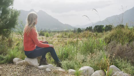 caucasian woman having a good time on a trip to the mountains, sitting on a rock, admiring the view