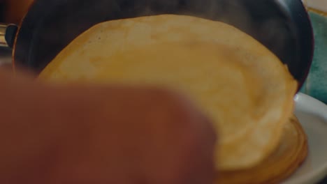 Warm-steamy-pancake-is-carefully-placed-on-plate-from-hot-pan-handheld-shot