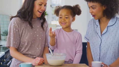 Familie-Mit-Zwei-Müttern-Im-Schlafanzug,-Die-Zu-Hause-Mit-Ihrer-Tochter-Morgenpfannkuchen-In-Der-Küche-Backen