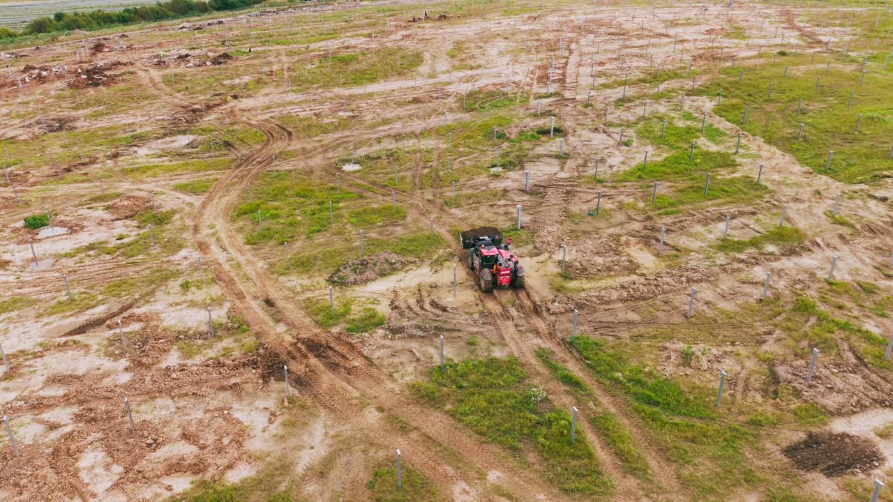 Drone segue trattore rosso che si muove attraverso un sito in fase iniziale di campo solare