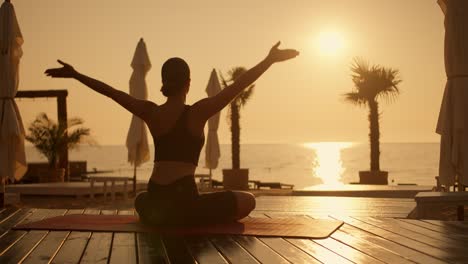 A-brunette-girl-in-a-black-top-sits-on-a-red-carpet-on-the-beach-and-takes-a-meditation-pose.-Namaste-pose-and-meditation