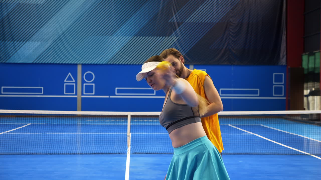 A man teaching a woman how to play pickleball in an inside court