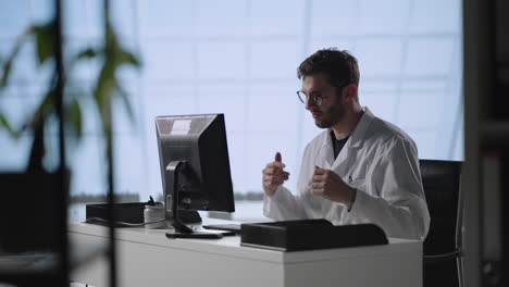 Imagen-Inclinada-Hacia-Abajo-De-Un-Médico-Masculino-Con-Bata-De-Laboratorio-Y-Gafas-Escribiendo-En-Una-Computadora-Portátil-Mientras-Trabaja-En-El-Escritorio-Del-Consultorio-Médico