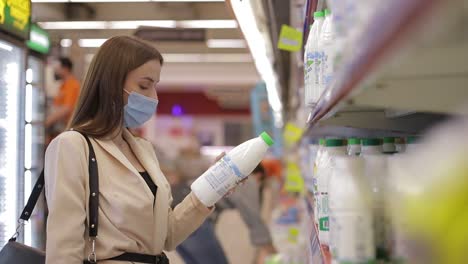 a young woman in a medical mask buys food in a supermarket during the covid-19 coronavirus epidemic. the woman stores food during quarantine and self-isolation. social video