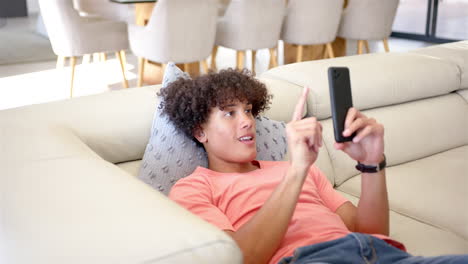 a young biracial man is lounging on sofa, smartphone in hand