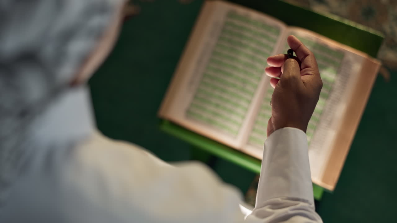 Uomo musulmano che legge il Corano con un rosario musulmano