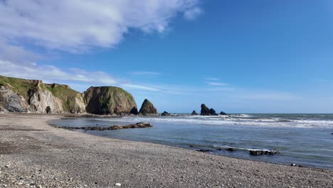 Playa-Desierta,-Acantilados-De-Guijarros-Y-Pilas-De-Mar-Con-Suaves-Olas-En-La-Laguna-Azul-En-Un-Día-De-Primavera-En-Waterford,-Irlanda