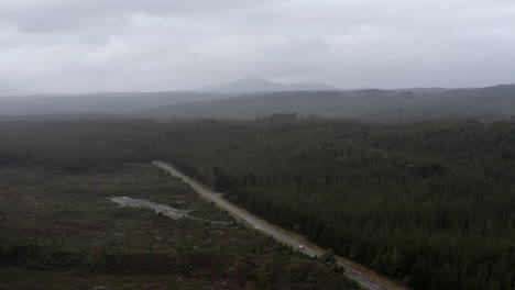 Aerial:-Car-driving-on-road-surrounded-by-trees,-mountains-and-wilderness-in-Tasmania,-Australia