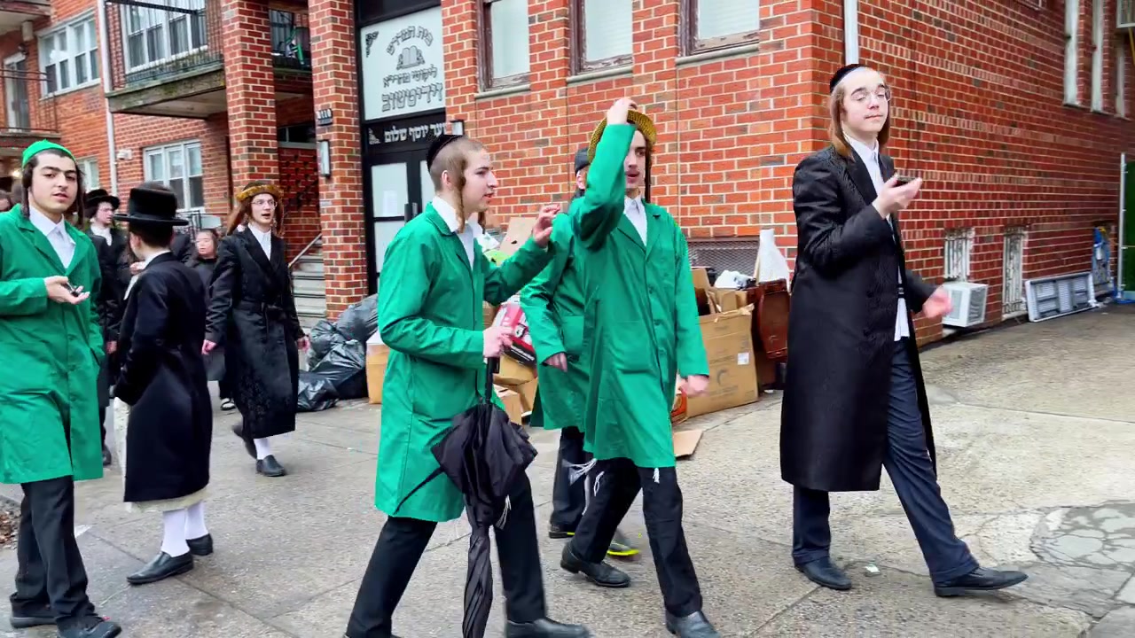 New York, USA, 9. marts 2022: Hasidiske mænd uden for bygning under et gadeevent. Hasidiske mænd og unge uden for murstensbygning med hebraisk skilt, kasser, smartphone og aktivitet på fortovet.