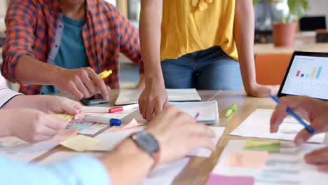 midsection of diverse colleagues brainstorming with documents and tablet in office in slow motion