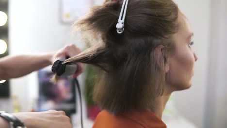 hairdresser straightens hair of sitting woman with a hair iron in beauty studio. she holds special appliance in hands and gently