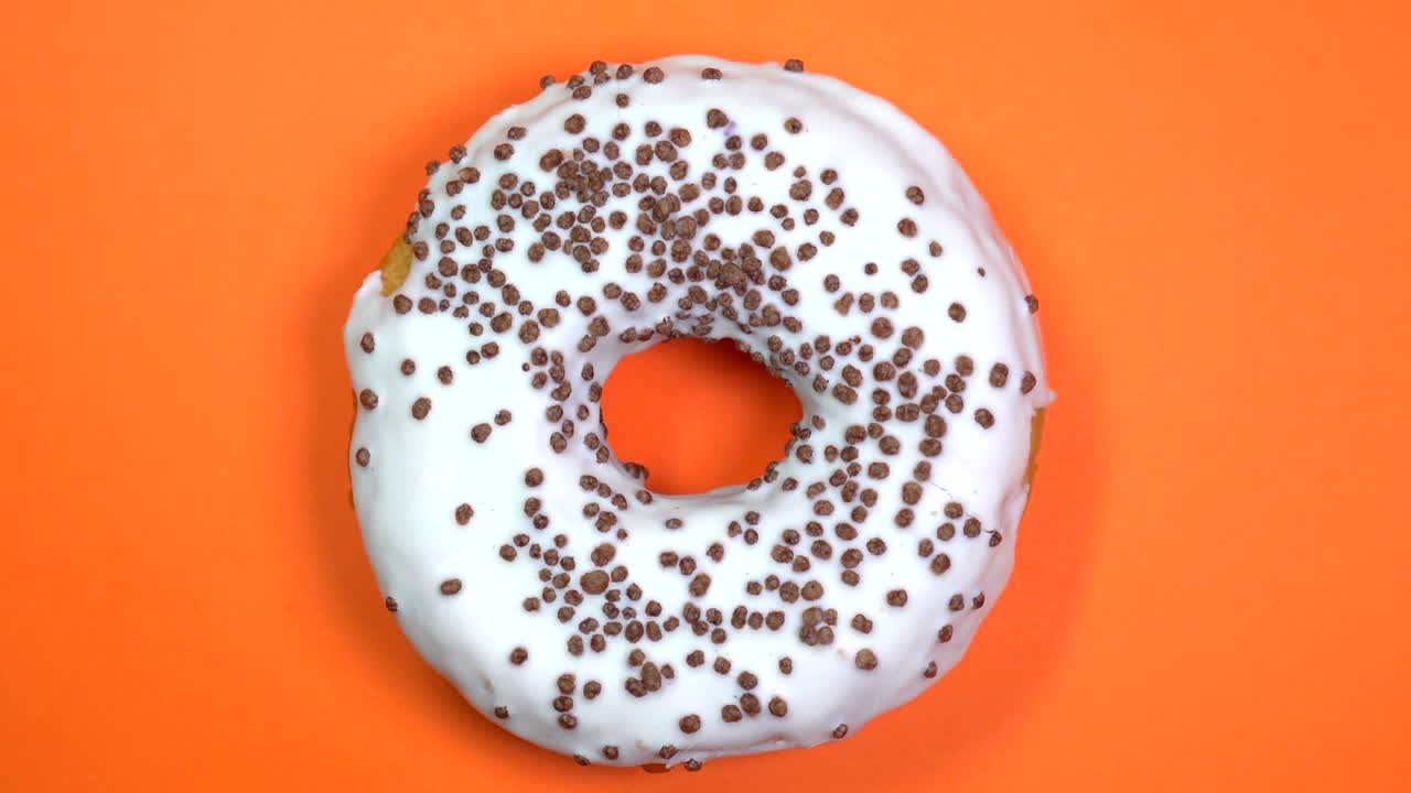 donut brillante y blanco con bolas de chocolate, macro disparado, girando sobre un fondo naranja.