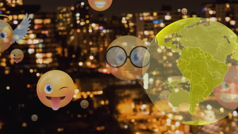 spinning globe and multiple face emoji icons floating against aerial view of cityscape at night