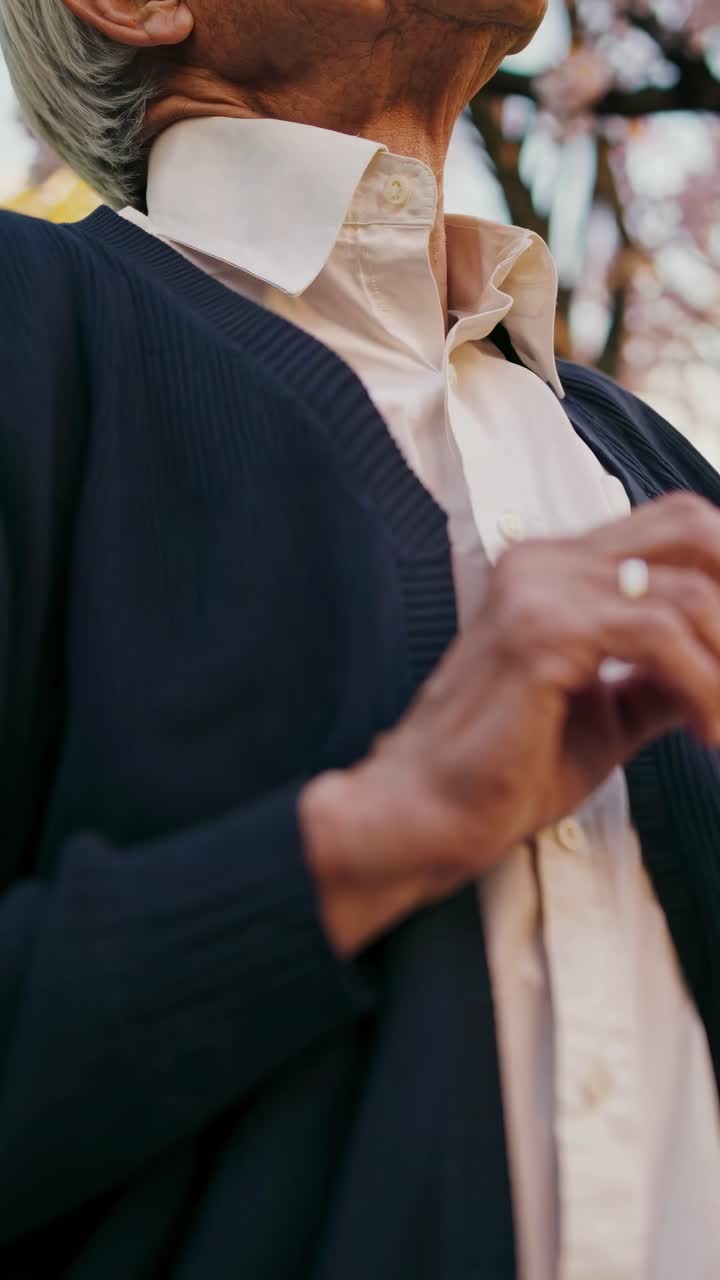 Ripresa video dal basso verso l'alto di una persona anziana con un cardigan blu scuro e una camicia bianca, che cattura una serena