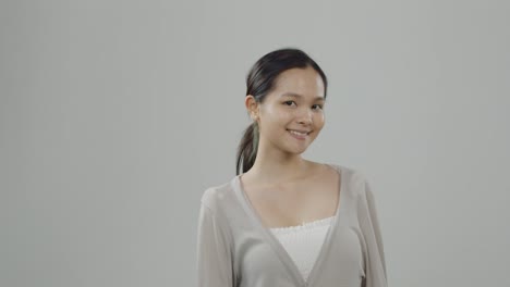 Linda,-Joven-Mujer-Asiática-Con-Suéter-Beige-Sobre-Camisa-Blanca-Y-Sin-Poses-De-Maquillaje-Y-Sonrisas-En-La-Audición-De-Casting---Pelo-Largo-Recogido-En-Una-Cola-De-Caballo