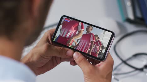 compuesto de un médico masculino viendo un partido de hockey en un teléfono inteligente