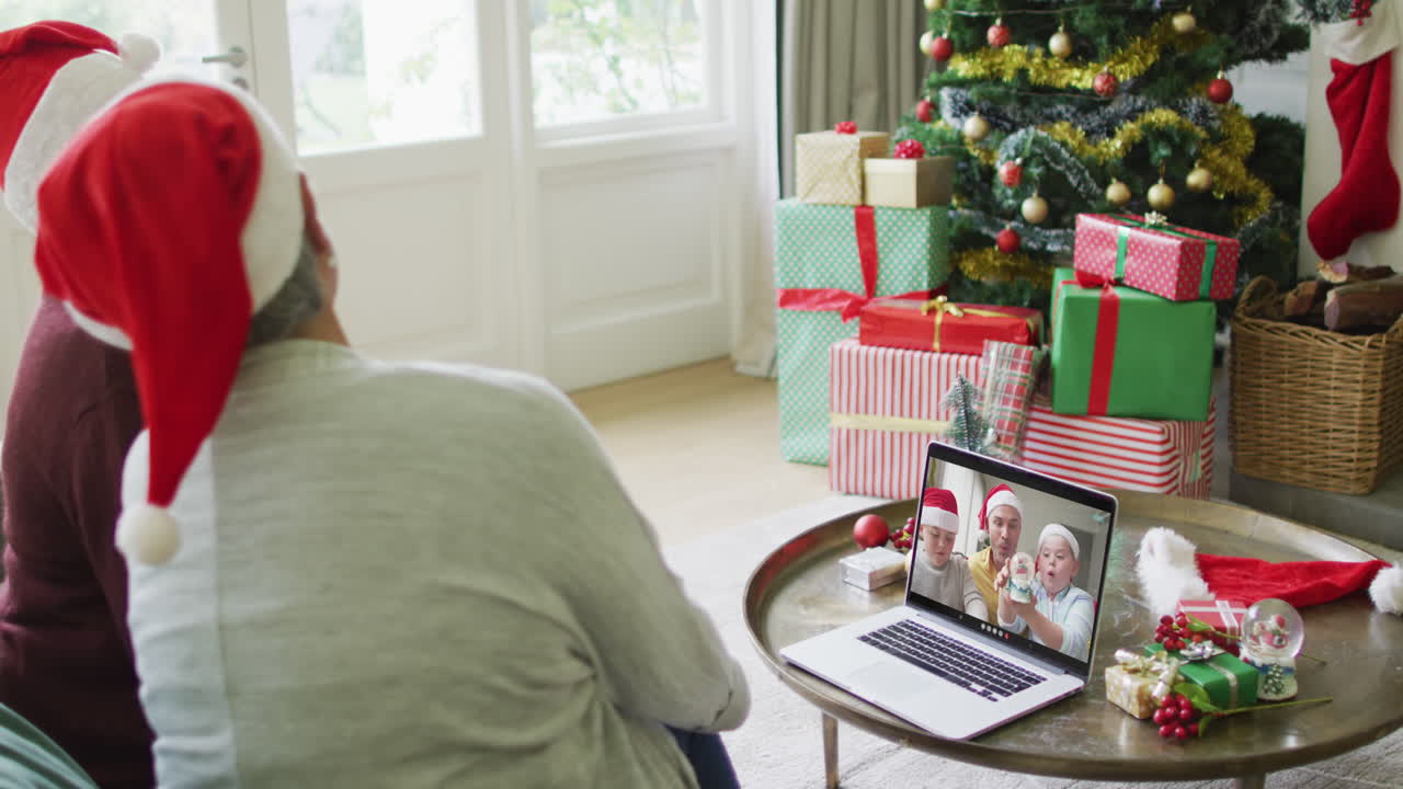 amigas mayores diversas usando una computadora portátil para una videollamada de navidad con una familia sonriente en la pantalla