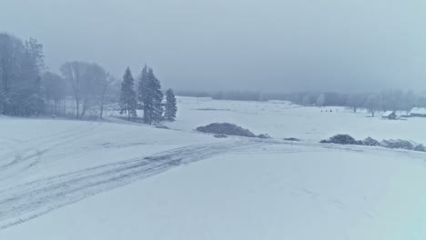 aerial drone shot over icy road and farmlands covered with snow while heavy snowing on a foggy winter day