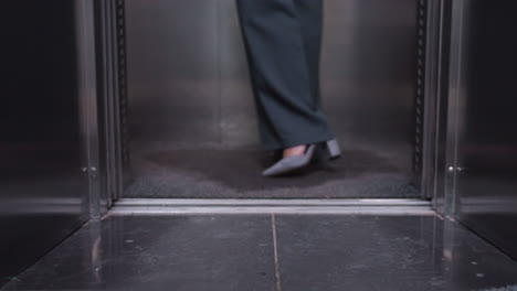 person stepping out of elevator wearing business attire, focus on legs and shoes, close-up shot showing steps in professional setting, office, movement in modern building interior