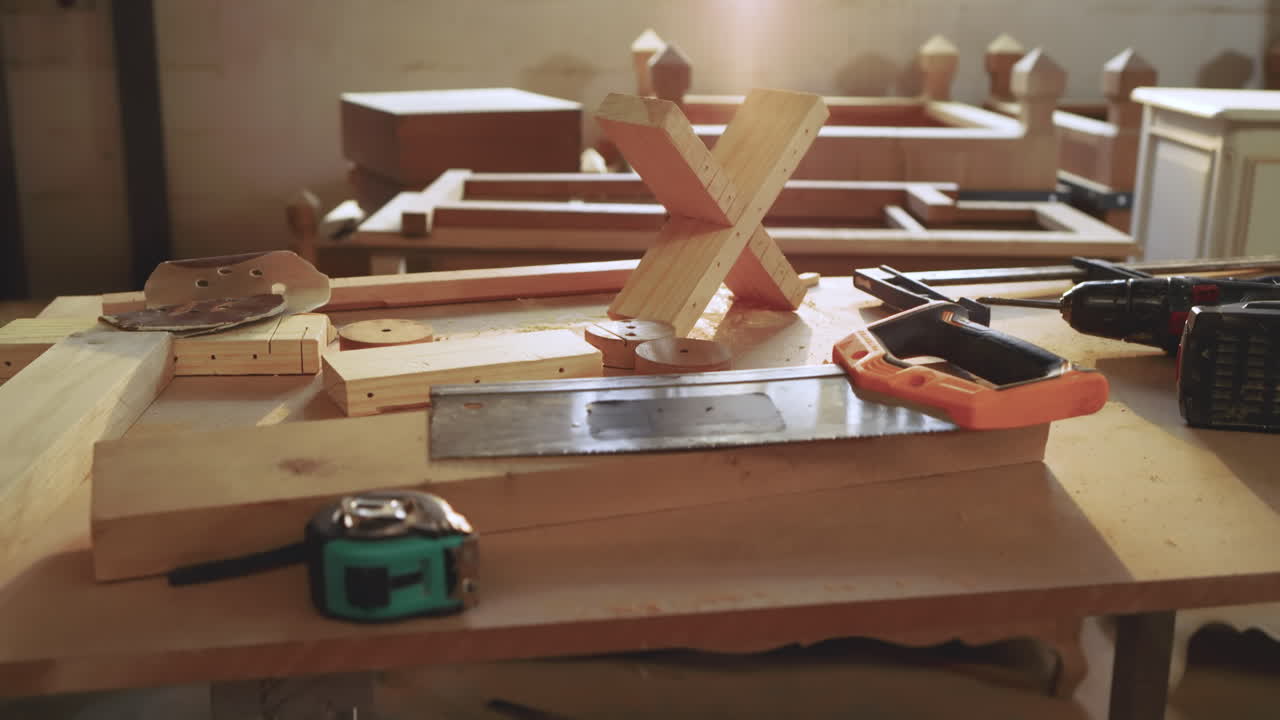 Upon start, camera is panning out to showcase drill, clamp, offcut planks on workbench under window