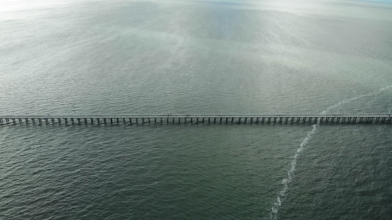 화창한 날에 어둡고 우울한 푸른 물이 넓게 펼쳐진 길고 나무 부두를 향해 카메라를 밀고 빠르게 기울입니다.