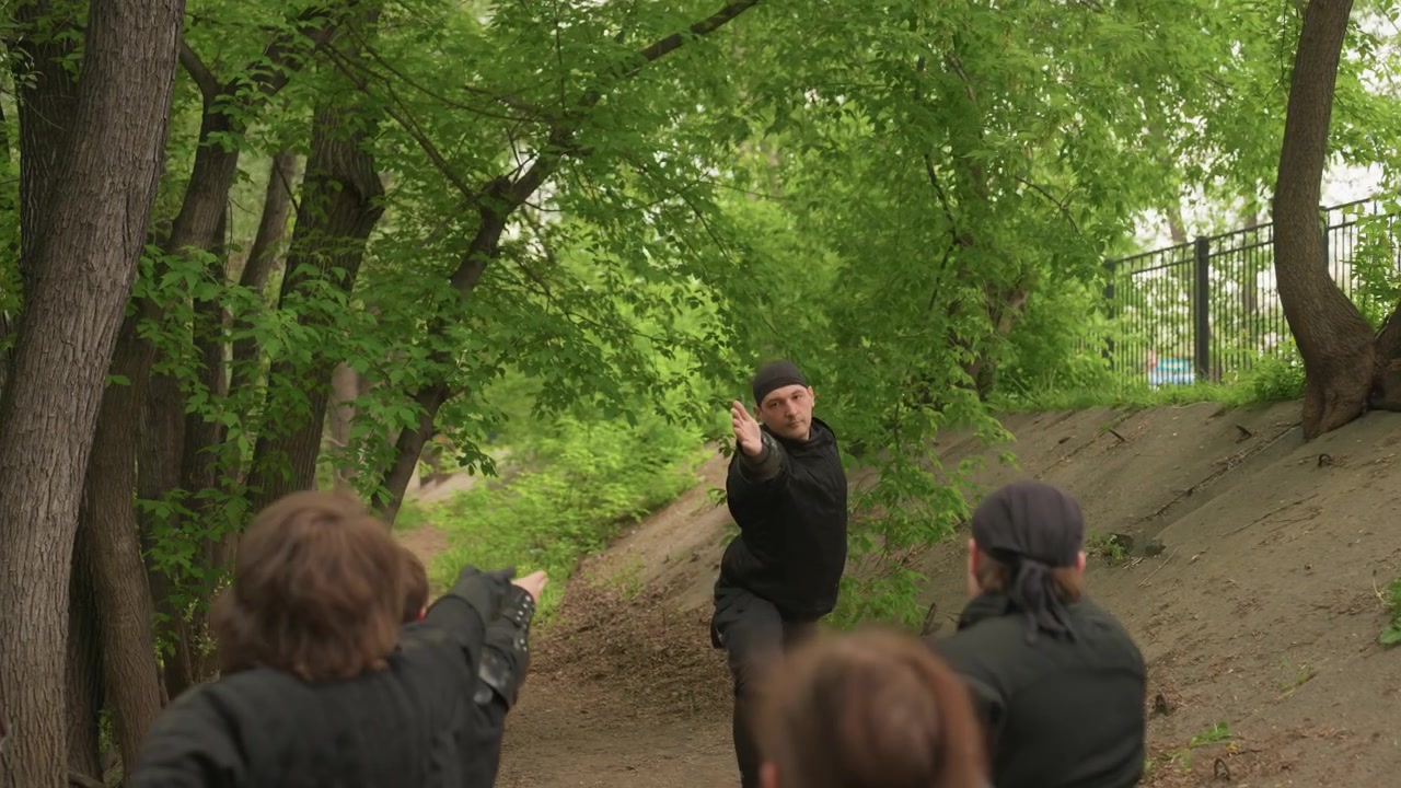 Primo piano di un uomo che dimostra tecniche di arti marziali a diversi studenti in un parco all'aperto. Il dimostratore esegue movimenti precisi delle mani mentre il gruppo segue attentamente i suoi movimenti.