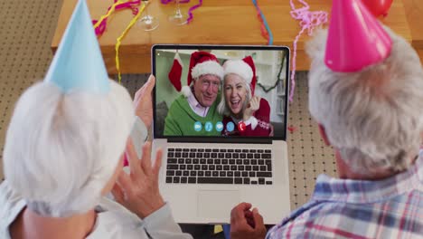 Caucasian-senior-couple-wearing-party-hats-on-laptop-video-chat-during-christmas-at-home