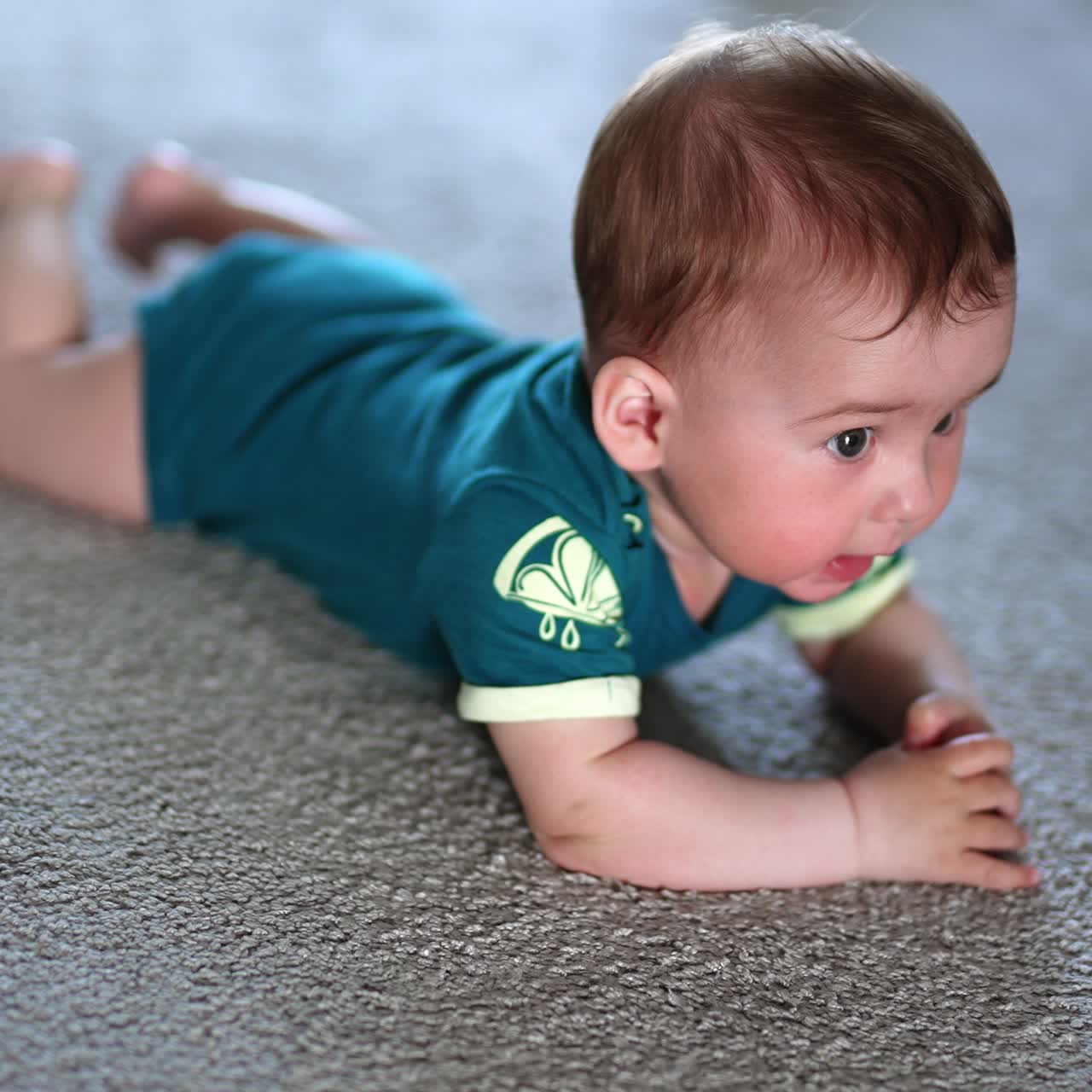Little child banging his hands over the floor happily. Beautiful kid lies on a carpet looking up with interest