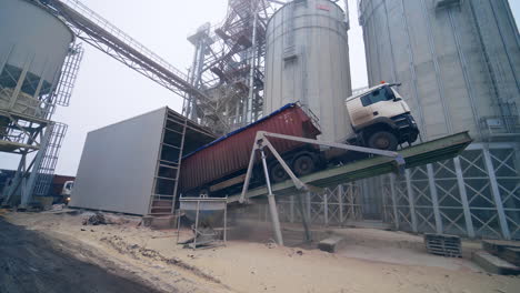 unloading grain from trailer to elevator for future storage. loaded truck on the lifting platform against the elevator tanks backdrop.