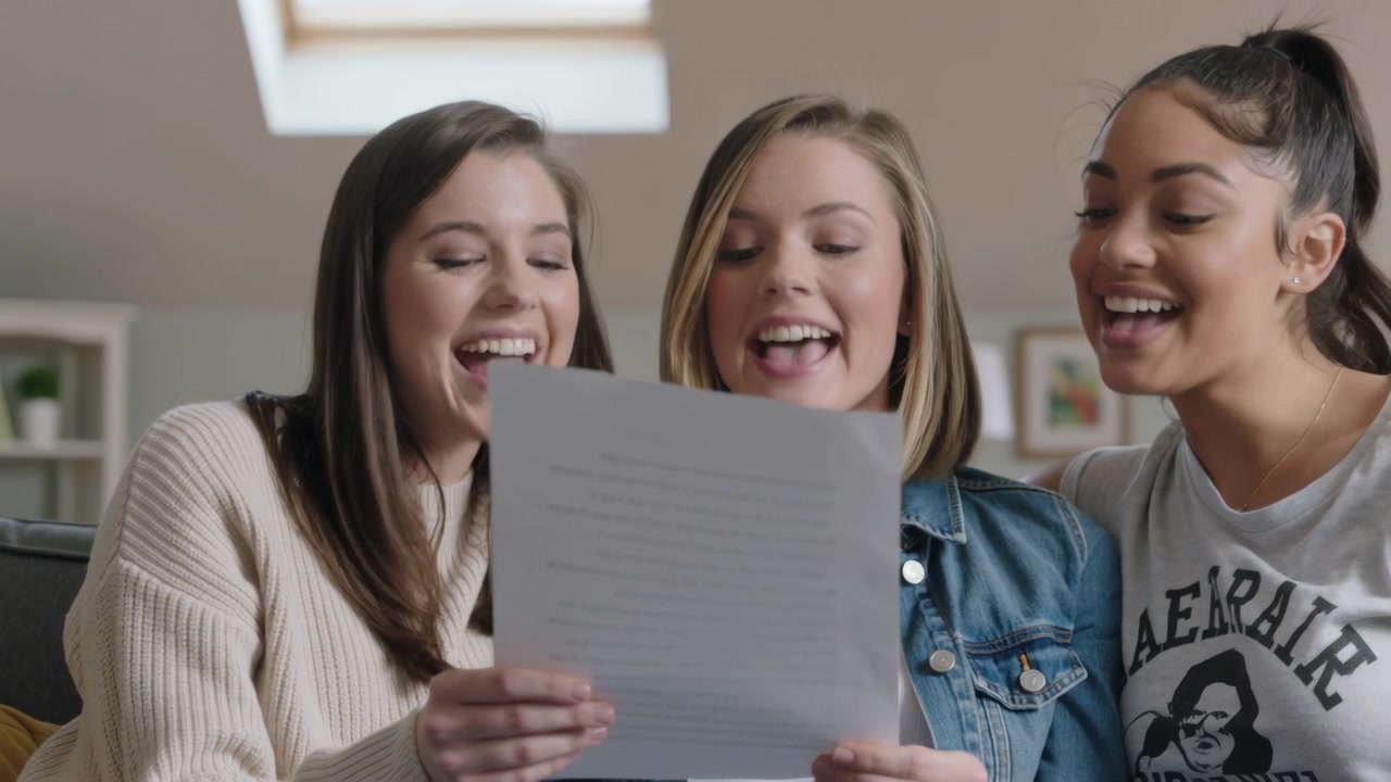 Tre donne in jeans leggono e cantano sul divano in un loft, tenendo un foglio e provando le battute.