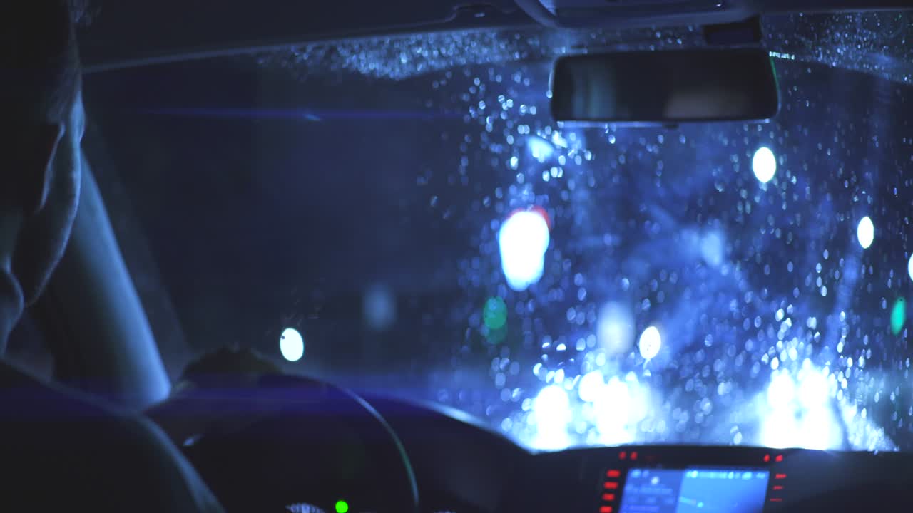 젊은이가 밤의 비가 오는 길을 따라 차를 운전합니다.