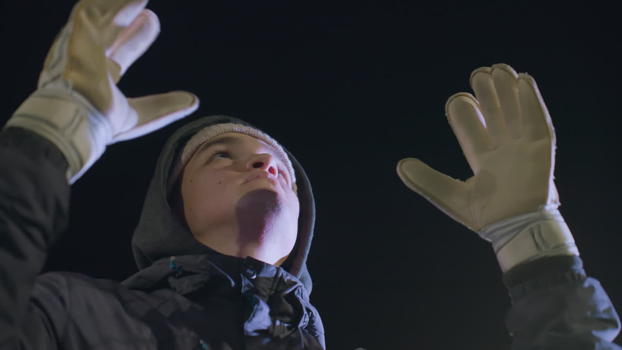 강렬한 훈련 중에 공을 잡는 장갑을 입은 축구 선수의 클로즈업, 모션 블러는 어두운 배경에 맞춰 액션과 초점을 강조합니다.